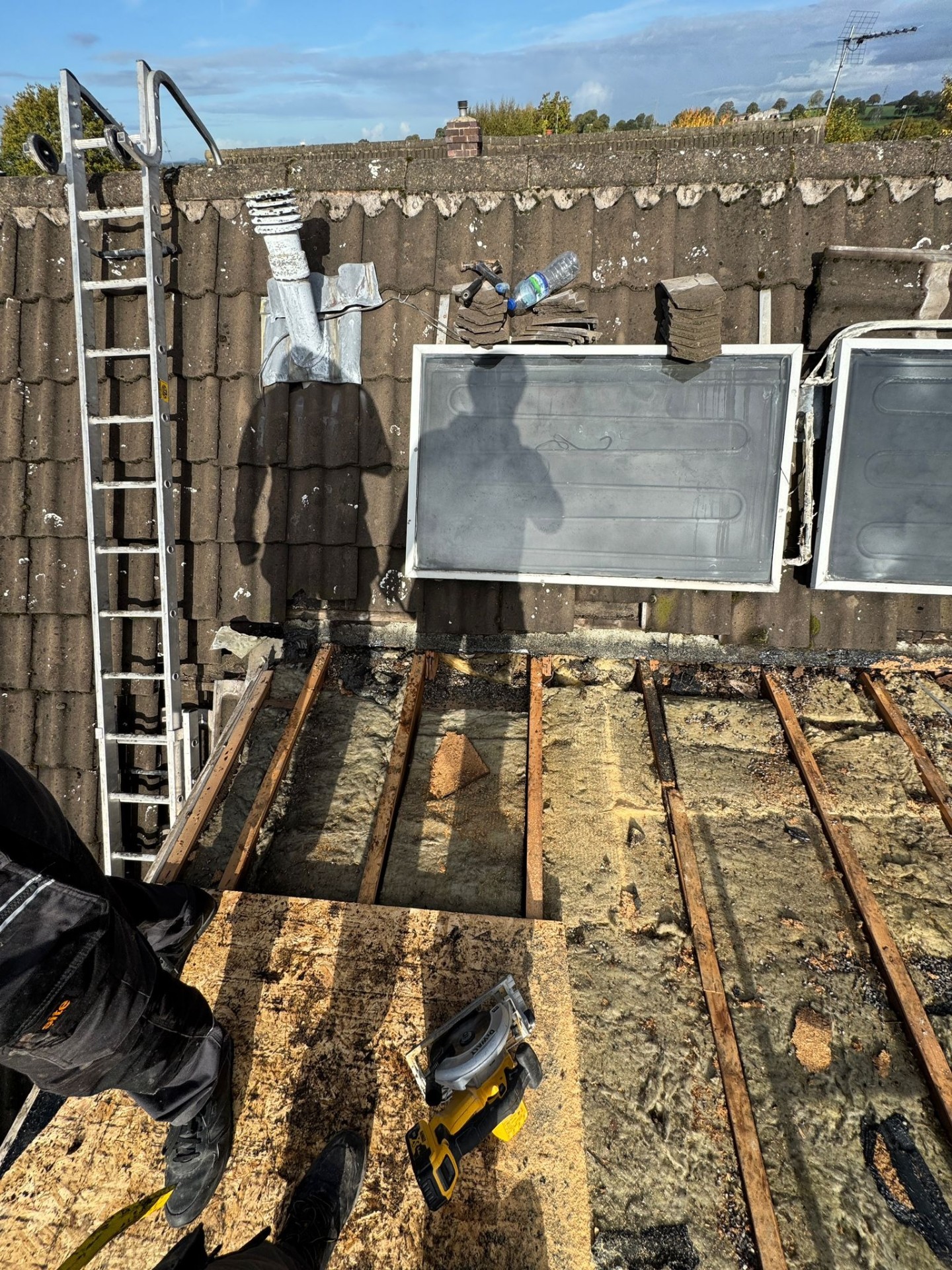 Storm-damaged roof showing exposed rafters and tiles being replaced during emergency repair