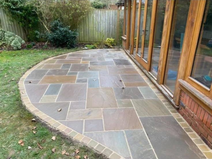Curved Indian sandstone patio with buff border running alongside a conservatory